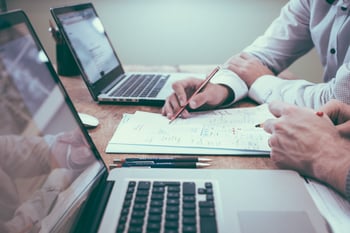 business professionals at desk with laptop, pens, and paper